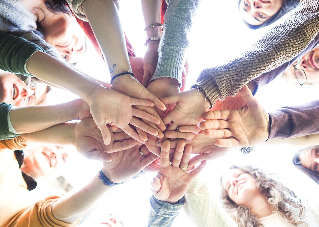 Eine Gruppe von Menschen, die ihre Hände in der Mitte zusammenlegen, symbolisieren Einheit und Zusammenarbeit.