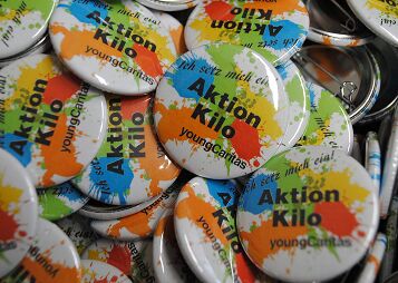 Viele bunte Ansteckbuttons mit Schrift Aktion Kilo und youngCaritas liegen zusammen
