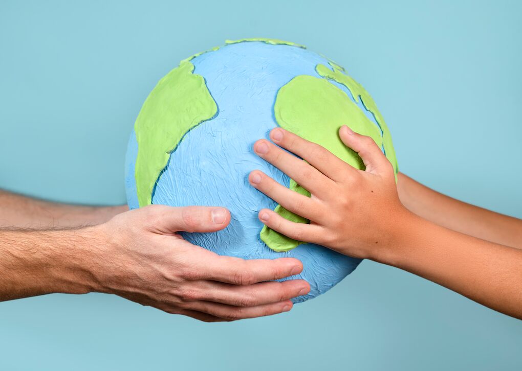 Eine Erwachsenenhands und einer Kinderhand halten gemeinsam eine Modellerde der Erde, Symbol für Zusammenarbeit und Verantwortung.