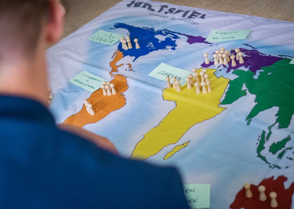 Eine Person schaut auf ein Brettspiel mit einer Weltkarte, auf der Figuren und Notizen platziert sind, die verschiedene Regionen markieren.