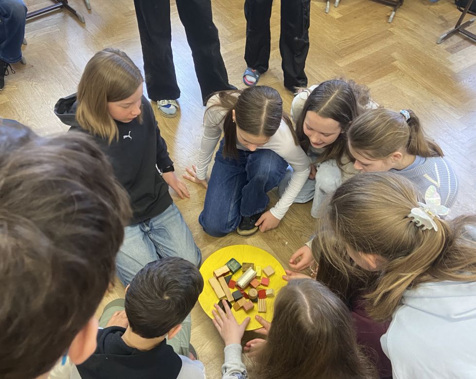 Eine Gruppe von Kindern sitzt auf dem Boden in einem Klassenzimmer und spielt mit bunten Bausteinen auf einem gelben Teller.