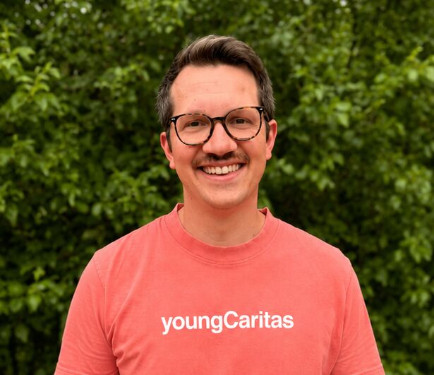 Ein junger Mann trägt ein lachsfarbenes T-Shirt mit der Aufschrift youngCaritas und lächelt