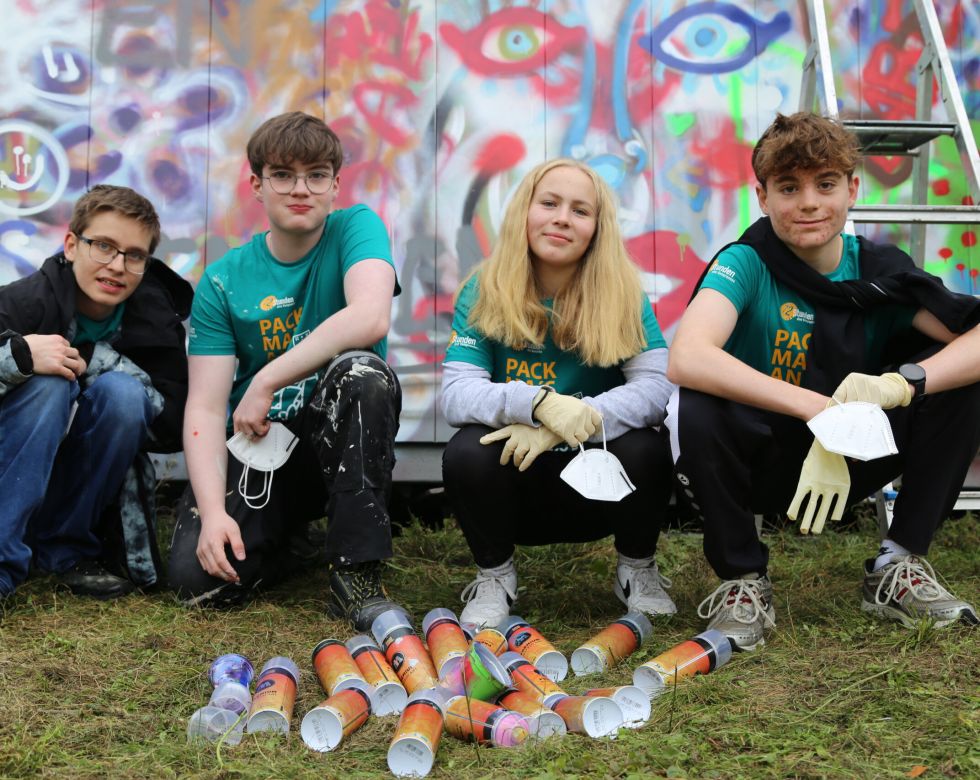 Gruppe von vier Jugendlichen, die an einem Kunstprojekt arbeiten, mit bunten Dosen und einem Graffiti-Hintergrund.