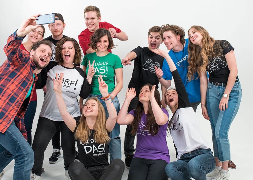 Gruppe junger Menschen, die fröhlich in die Kamera lächeln und hoch die Hände halten, während sie ein Selfie machen