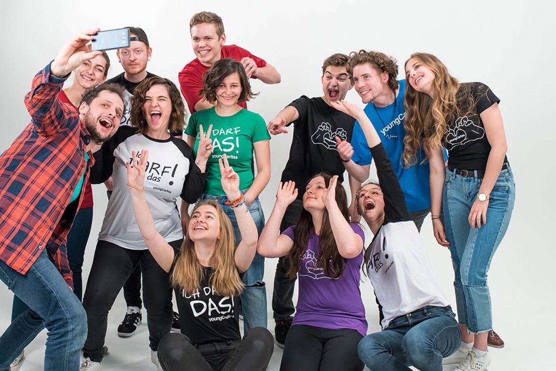 Gruppe junger Menschen, die fröhlich in die Kamera lächeln und hoch die Hände halten, während sie ein Selfie machen