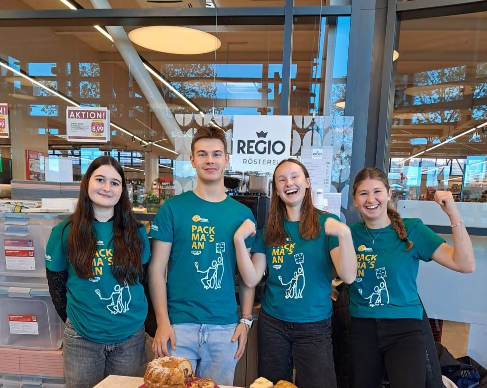 Vier junge Menschen in passenden grünen T-Shirts stehen lächelnd vor einem Geschäft.