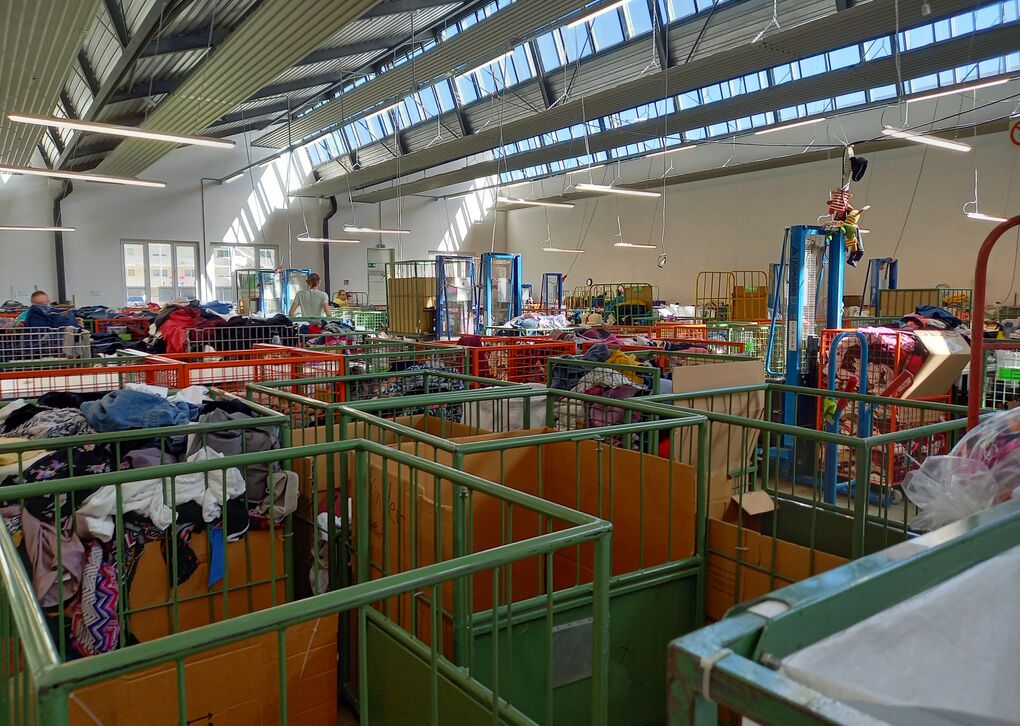Helles, großzügiges Bekleidungsgeschäft mit Aufbewahrungskisten voller Kleidung und Kunden, die stöbern.
