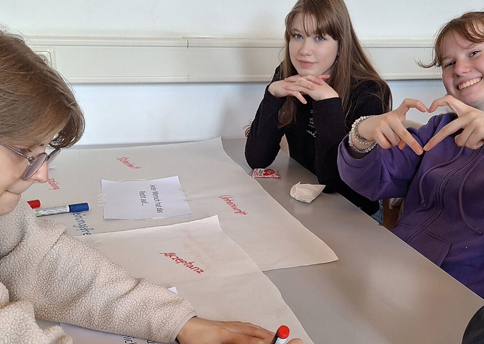 Drei Jugendliche sitzen an einem Tisch und arbeiten gemeinsam an einem Projekt mit Papier und Stiften