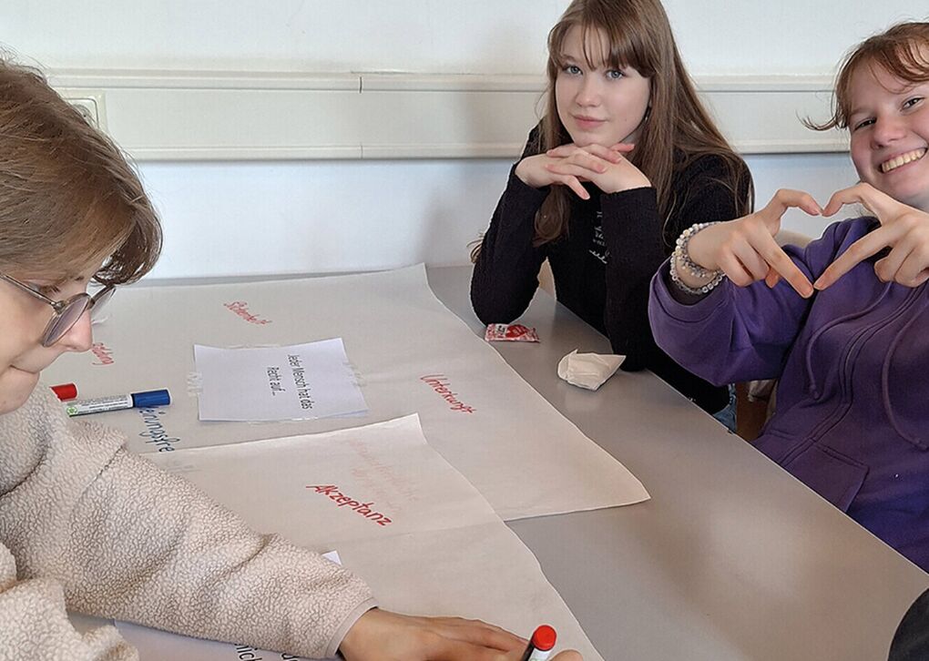 Drei Jugendliche sitzen an einem Tisch und arbeiten gemeinsam an einem Projekt mit Papier und Stiften
