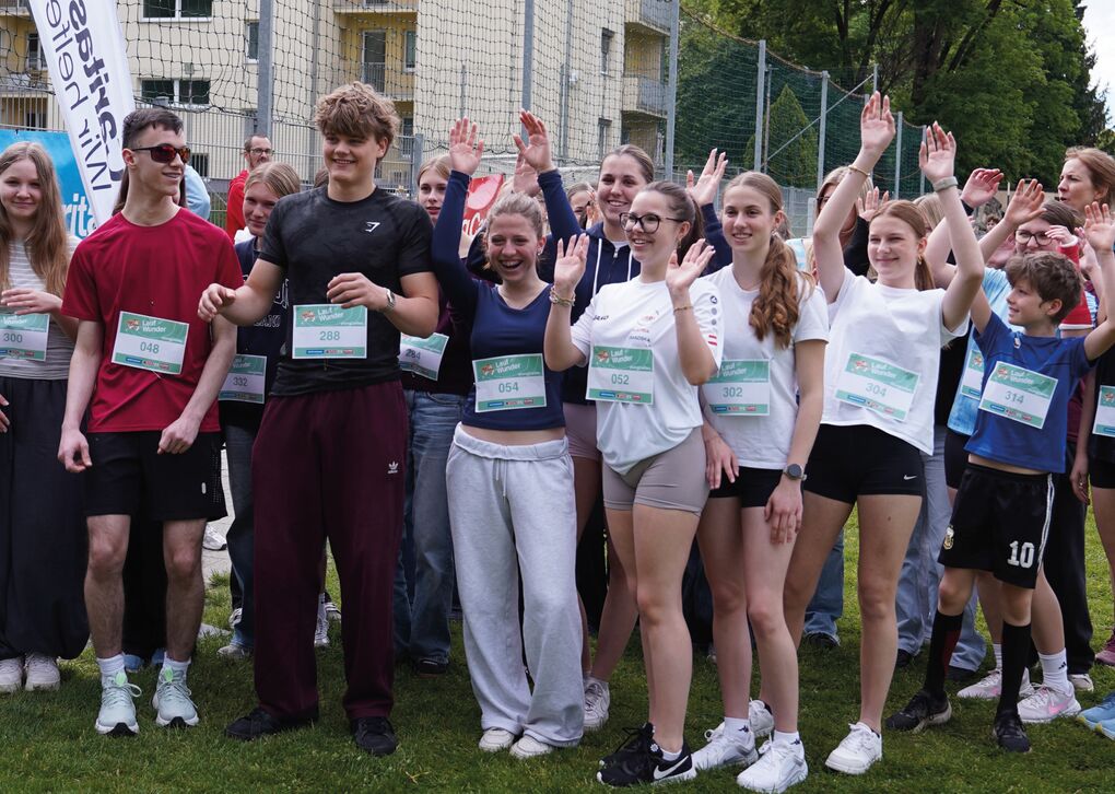 Schüler*innen in Laufkleidung heben die Arme. Sie stehen auf einer Laufbahn, rechts und links von ihnen sind Flaggen mit dem Caritas-Logo.