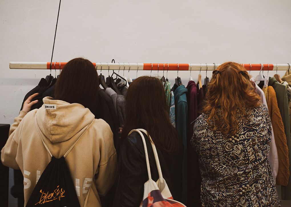 Drei Frauen stehen vor einem Kleiderständer und durchsuchen verschiedene Kleidungsteile.