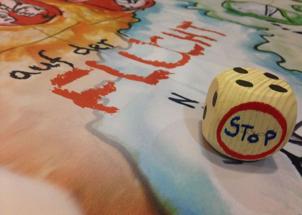 Nahaufnahme eines Holzspielwürfels mit der Aufschrift 'STOP' auf einem farbenfrohen Spielbrett.